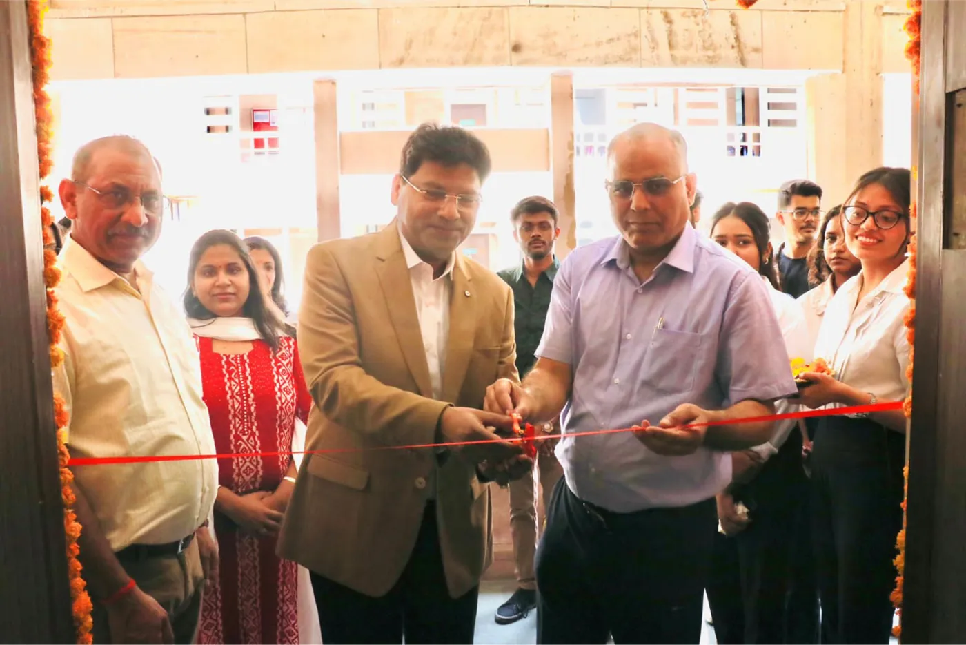 Two guests cutting the ribbon across a marigold-garlanded lab doorway, watched by staff and students