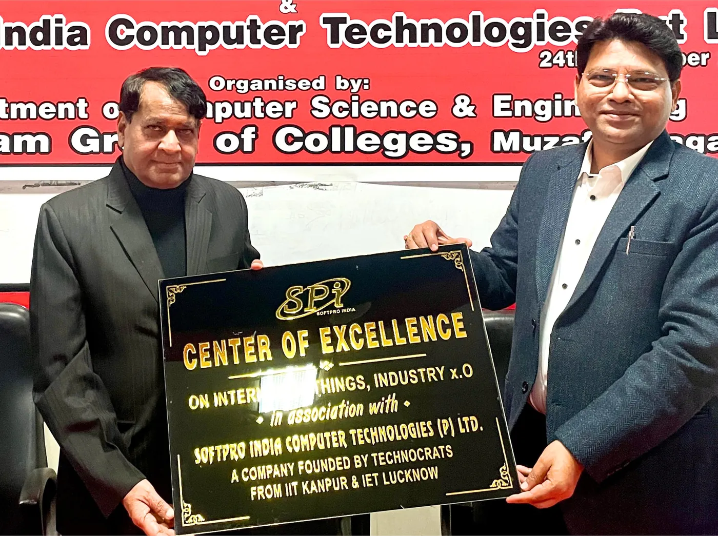 Two men holding the Center of Excellence name plate in front of the event banner