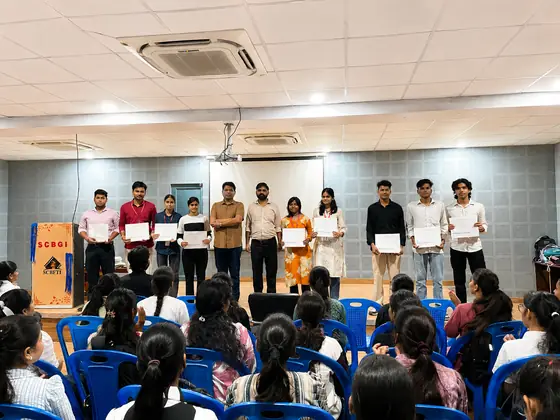 A line of students on stage holding their certificates up to the hall