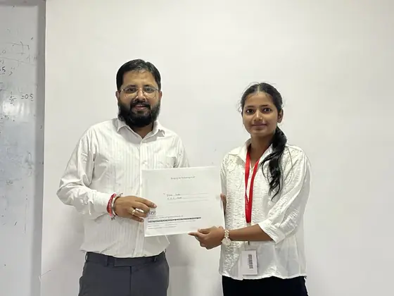 A trainer presenting a certificate to a student against a plain wall
