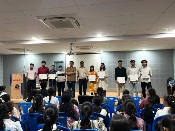 A row of students on stage with certificates, the seated hall in the foreground