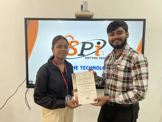A student receiving her certificate in front of the Softpro India screen