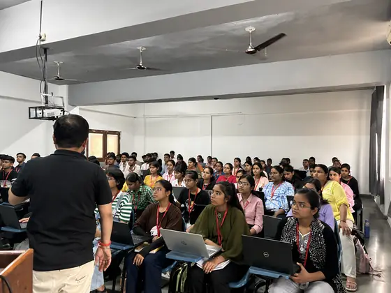 A Softpro trainer facing rows of students, several of them following along on laptops