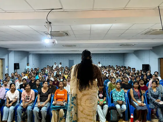 A trainer seen from behind, facing the seated rows of a college auditorium