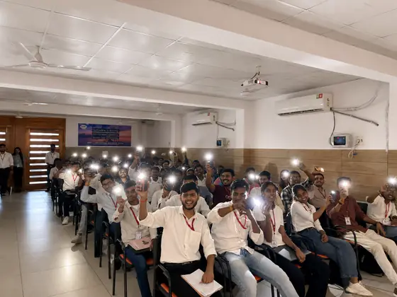 Students holding phone torches up in a darkened hall at the end of a session