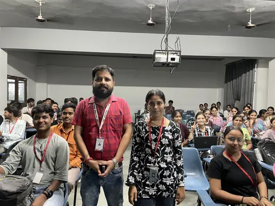 A trainer standing with students in a classroom, the batch seated around them