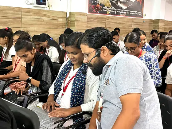 A trainer leaning over a laptop to help, students crowding round the screen