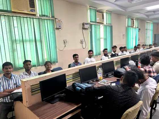 A computer lab with long benches of monitors, students seated along both sides