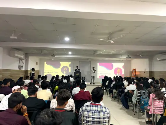 A speaker at the front of a hall with colourful slides projected behind them